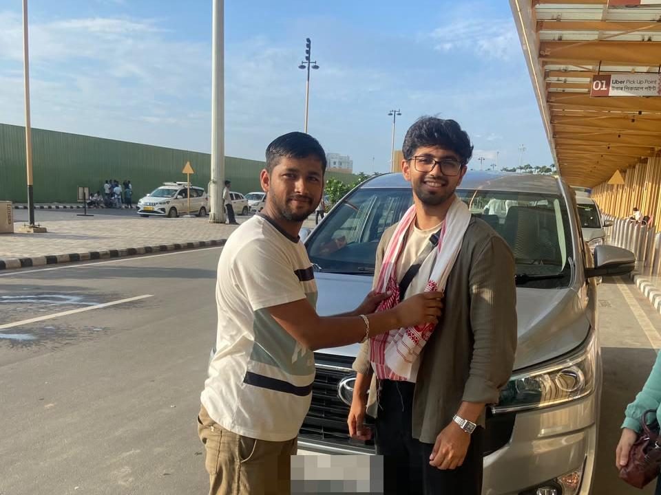 A Happy Yatra Travels guest welcomed with a traditional Assamese gamosa beside the Innova Crysta at Guwahati airport