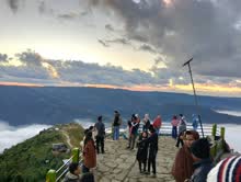 Travellers gathered at a railing watching the sunset over cloud-filled Meghalaya valleys